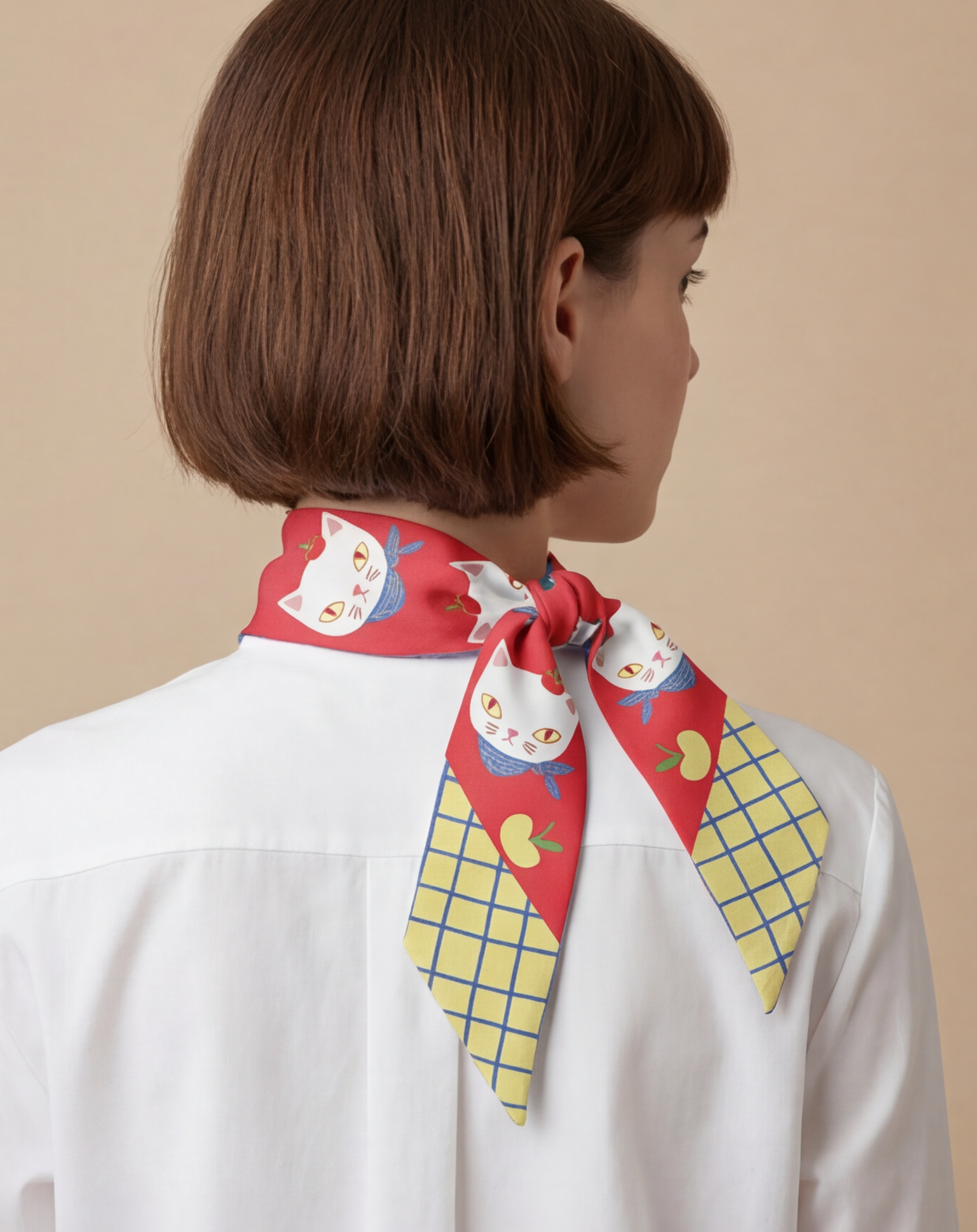 Person wearing a red and yellow twilly silk scarf with cats and apples on a beige background
