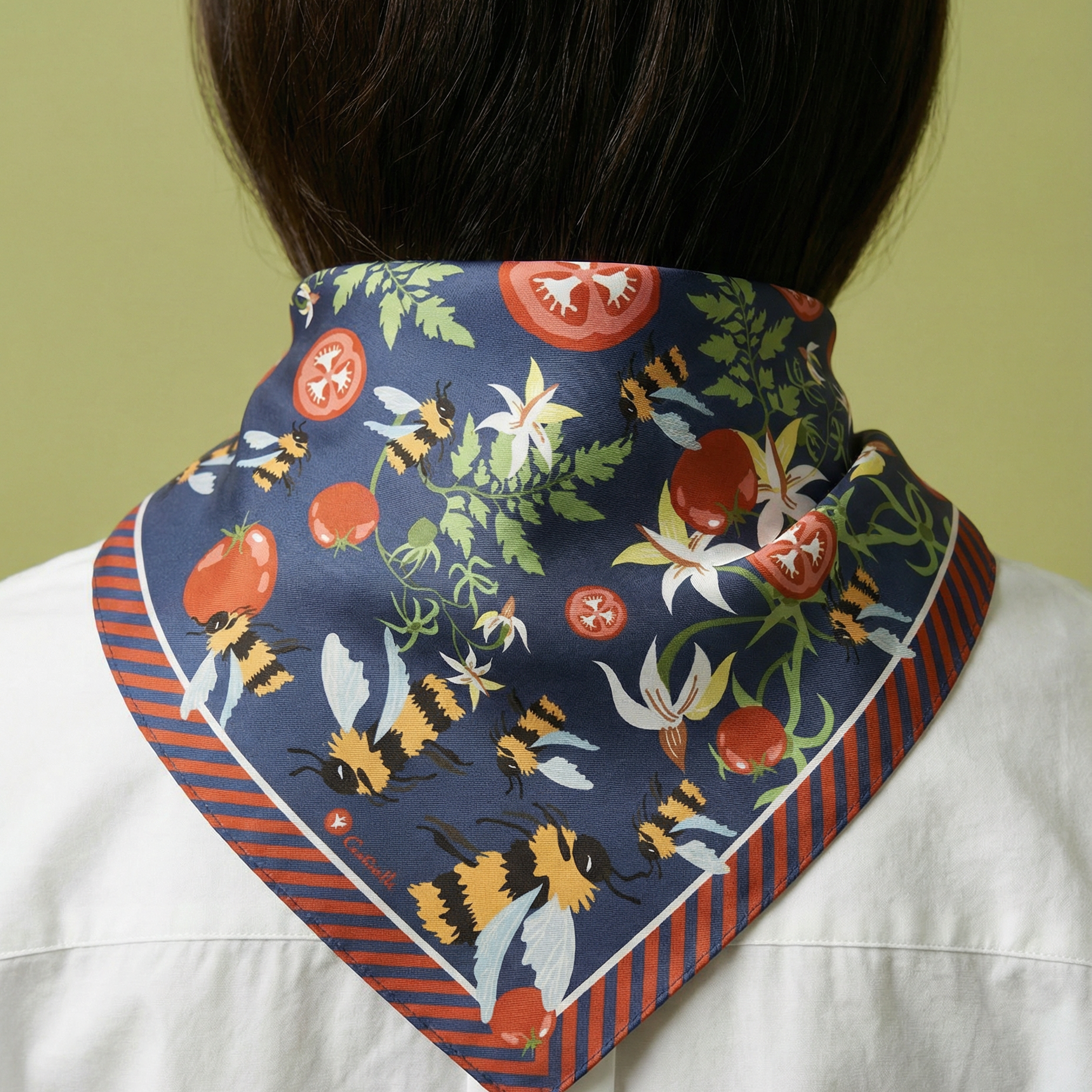 Person wearing a colorful scarf with floral and tomatoes and bumblebees pattern on a white shirt against a green background