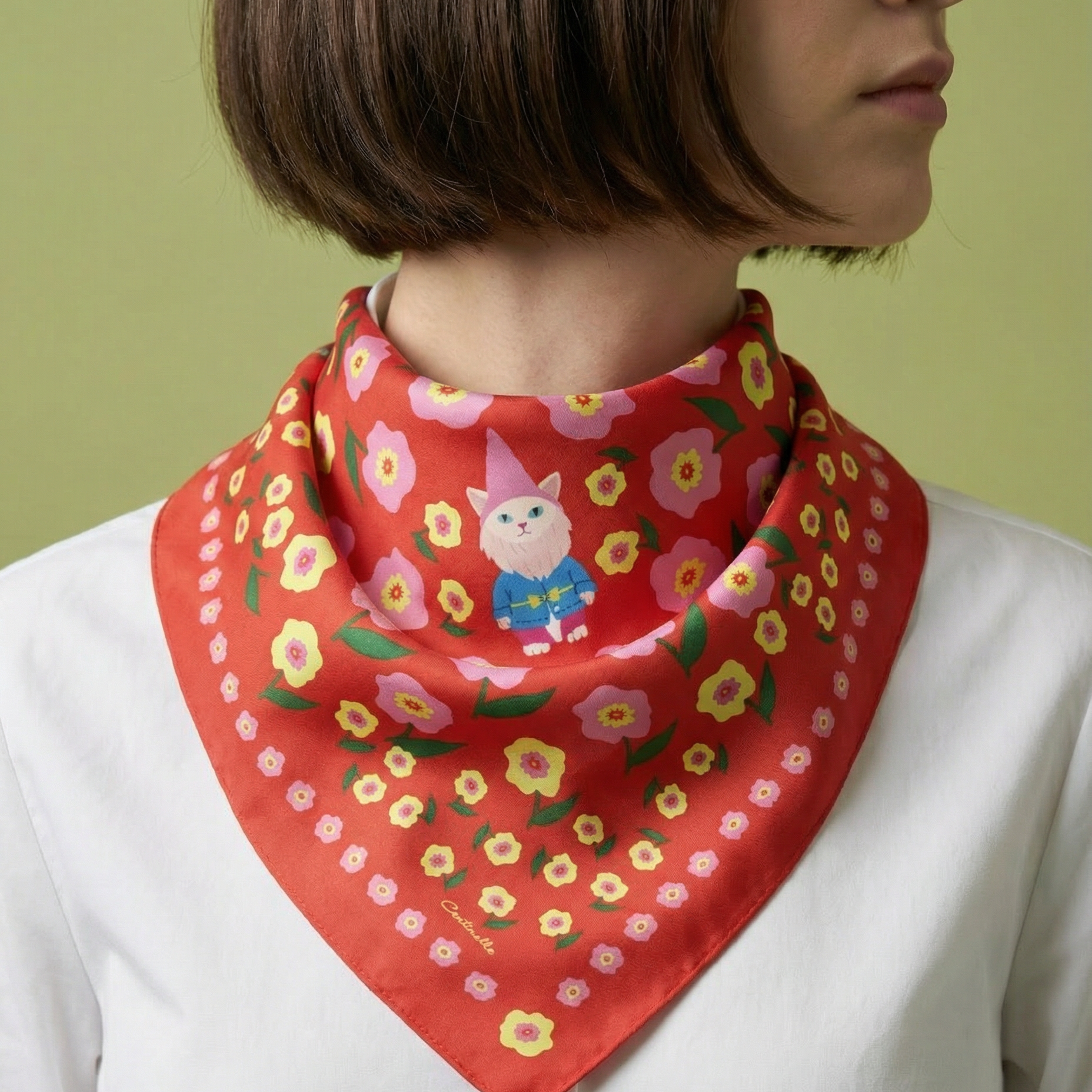 Person wearing a red floral scarf with a cat garden gnome illustration on a green background
