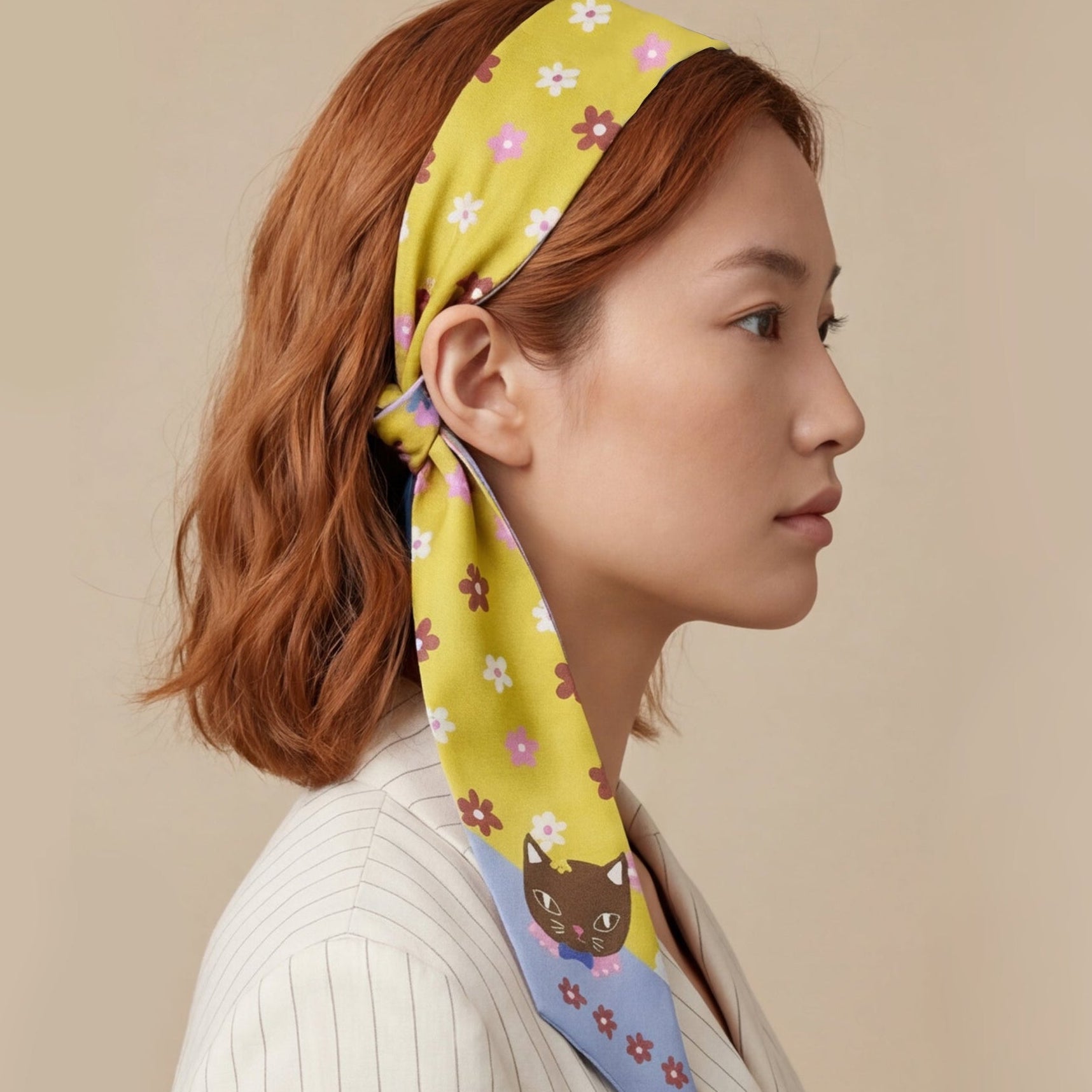 Woman wearing a colorful twilly silk scarf as headband with a cat design on a beige background