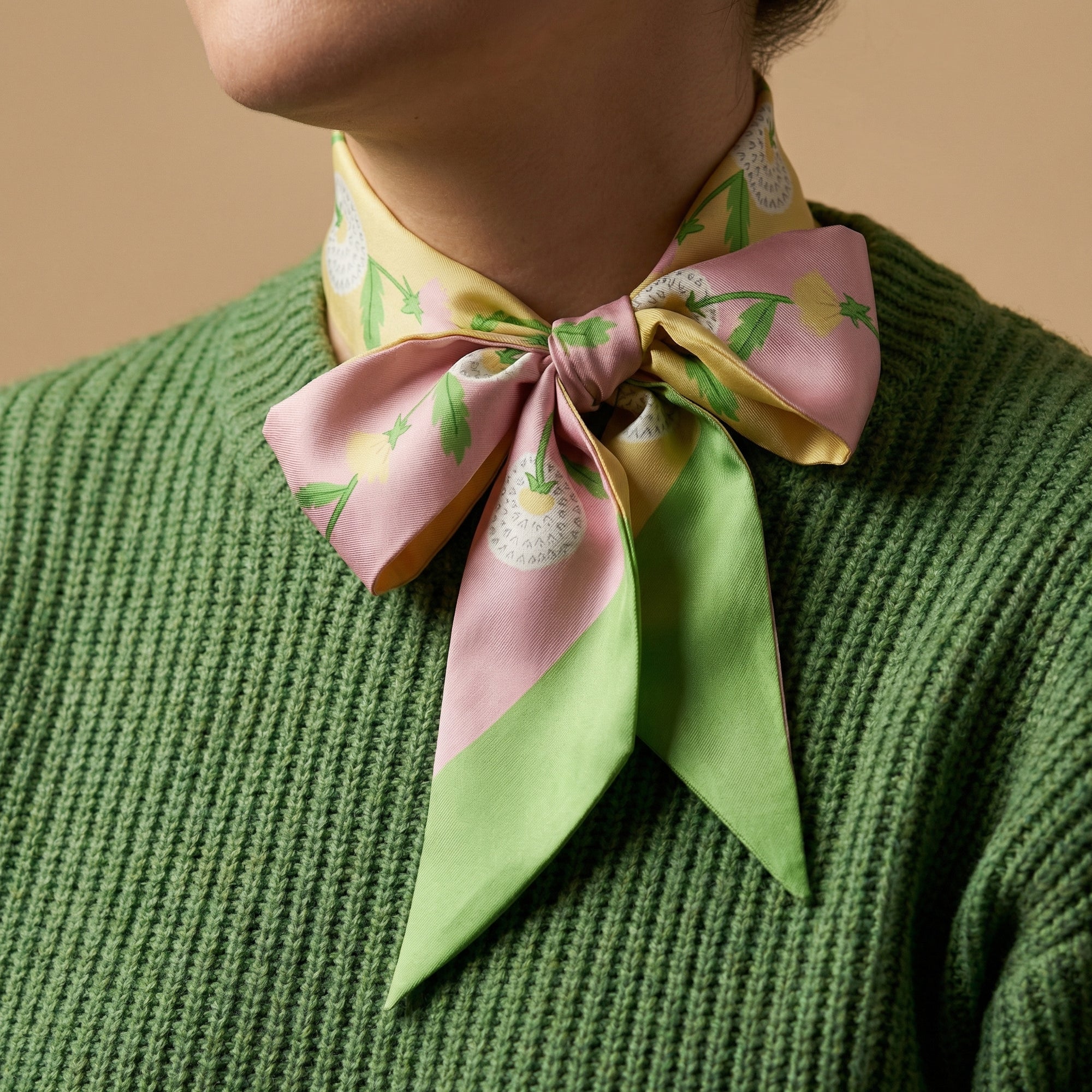 Person wearing a colorful twilly dandelion floral scarf tied around their neck against a beige background