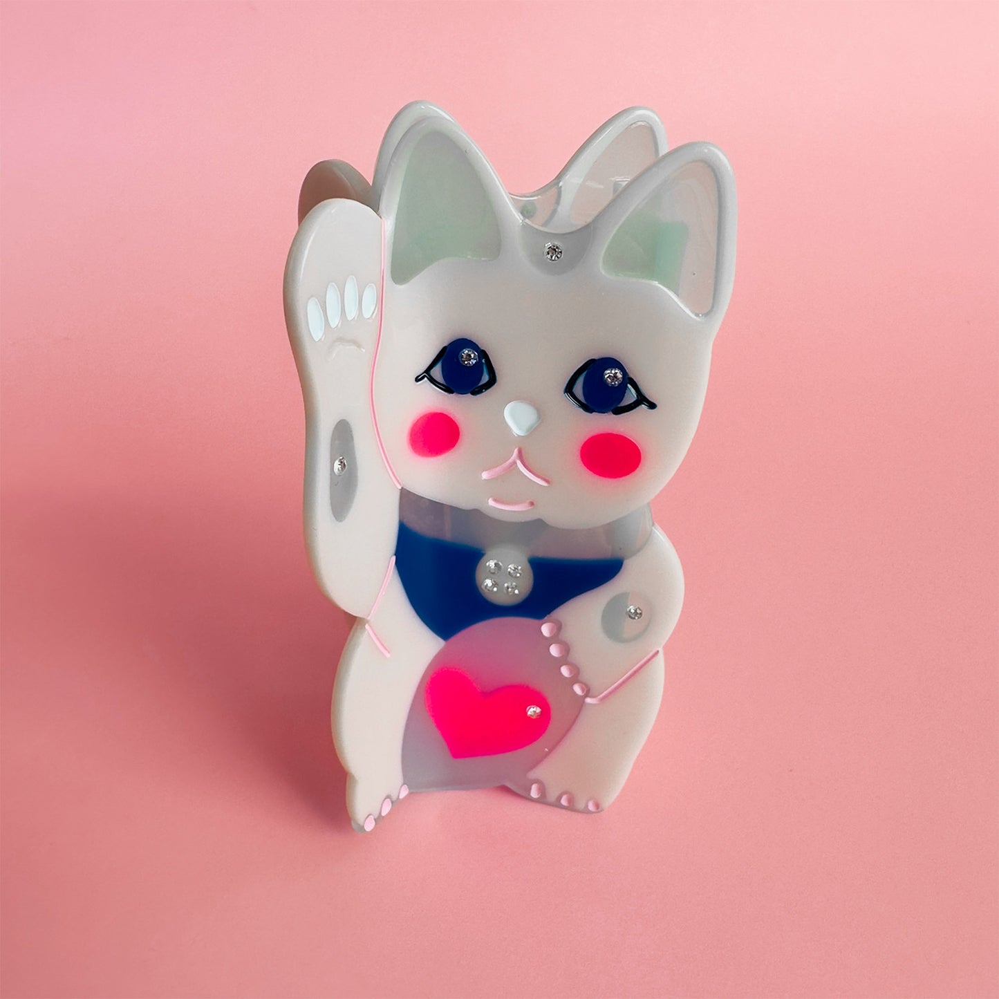 A maneki-neko white cat hair claw with a pink heart on a pink background.