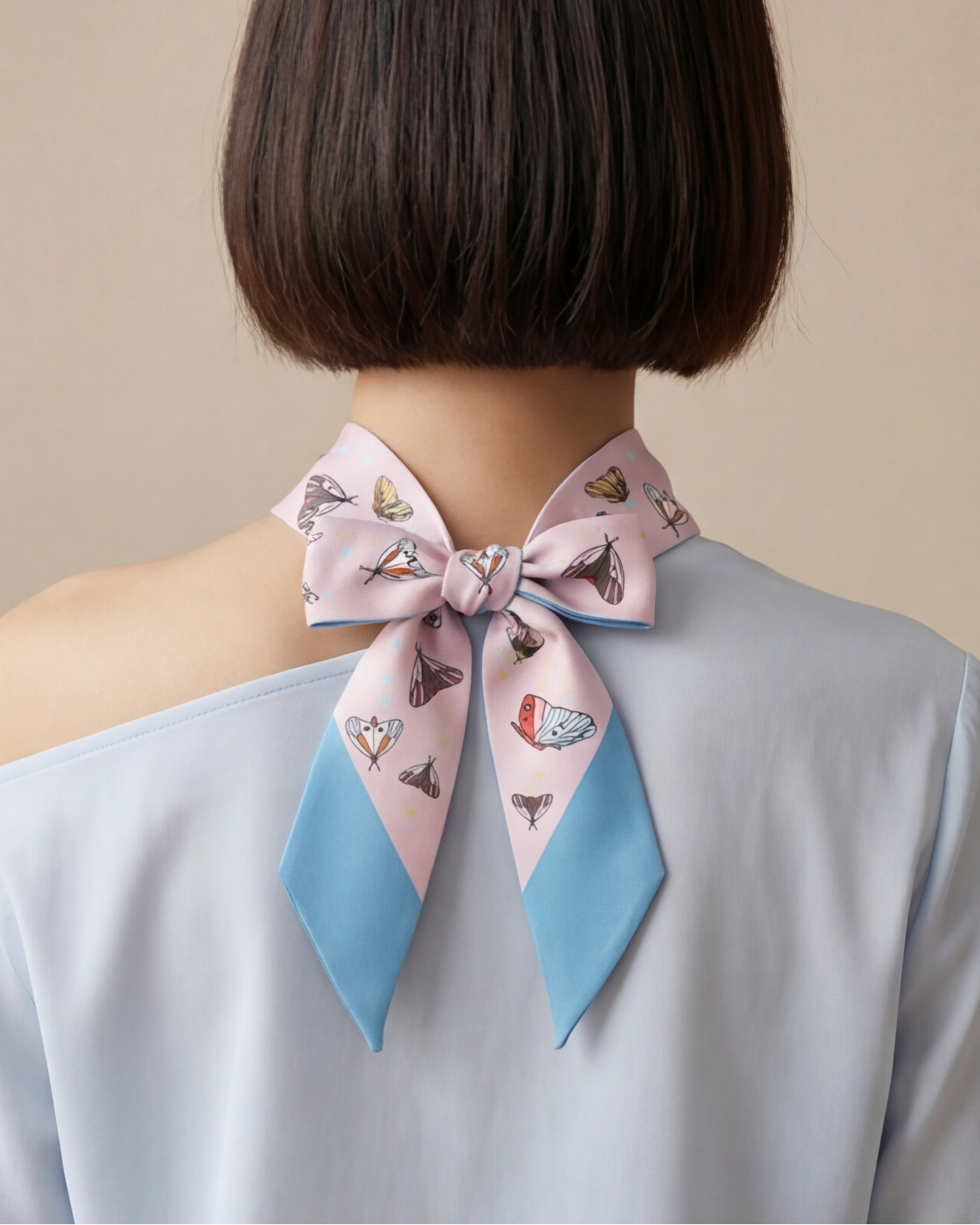 Person wearing a pink and blue patterned with butterflies and gourds scarf around their neck against a beige background