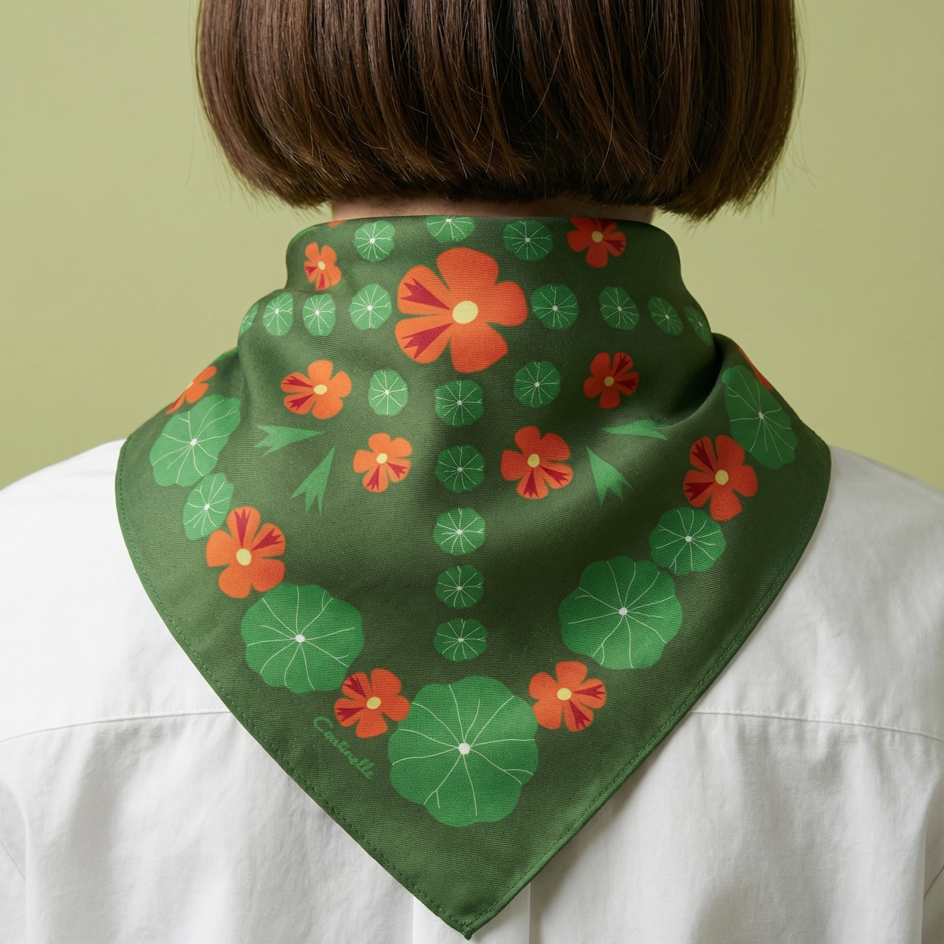 woman wearing a green scarf with orange nasturtium floral patterns on a plain background
