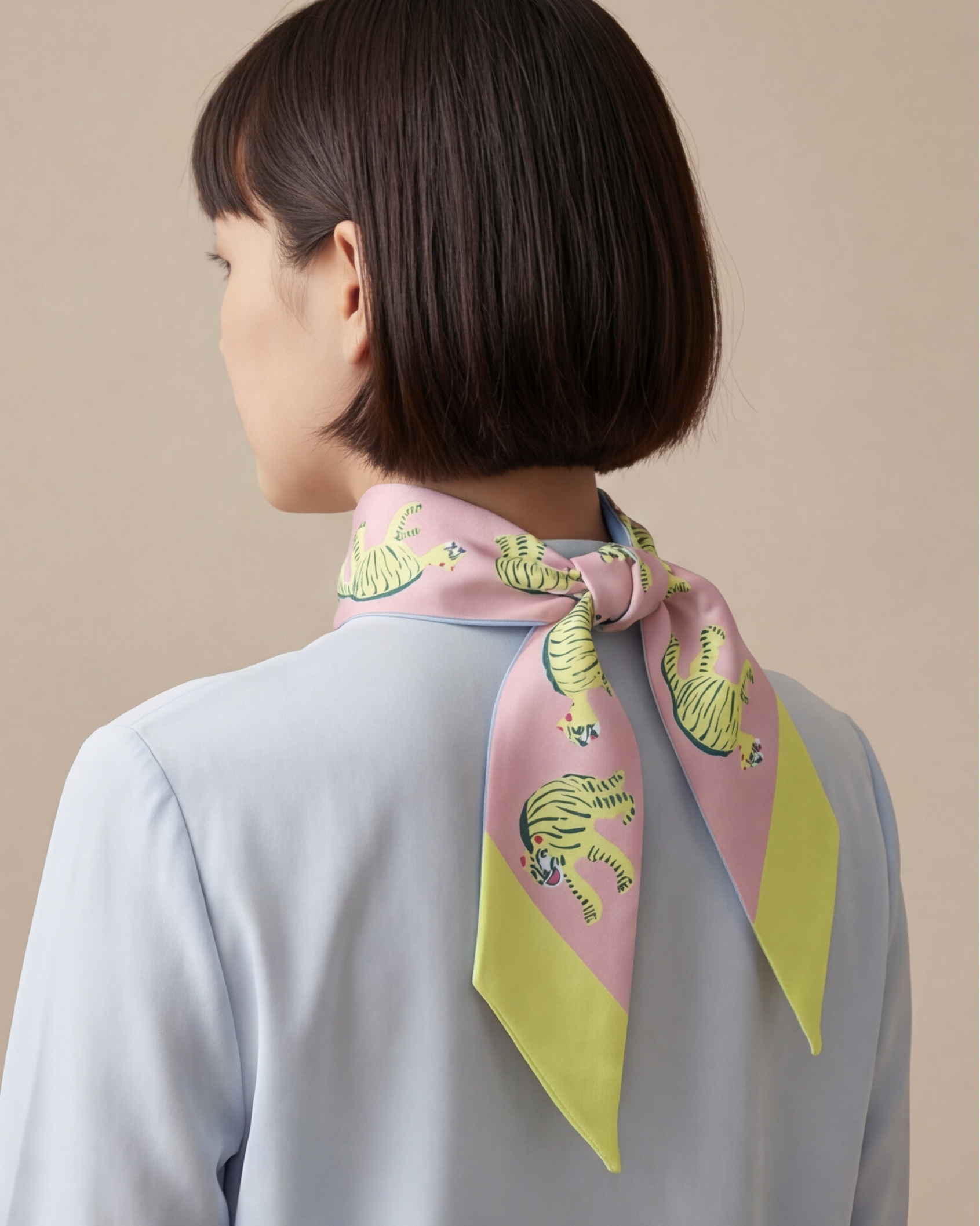Person wearing a colorful twilly silk scarf with a pink and yellow tigers design on a beige background