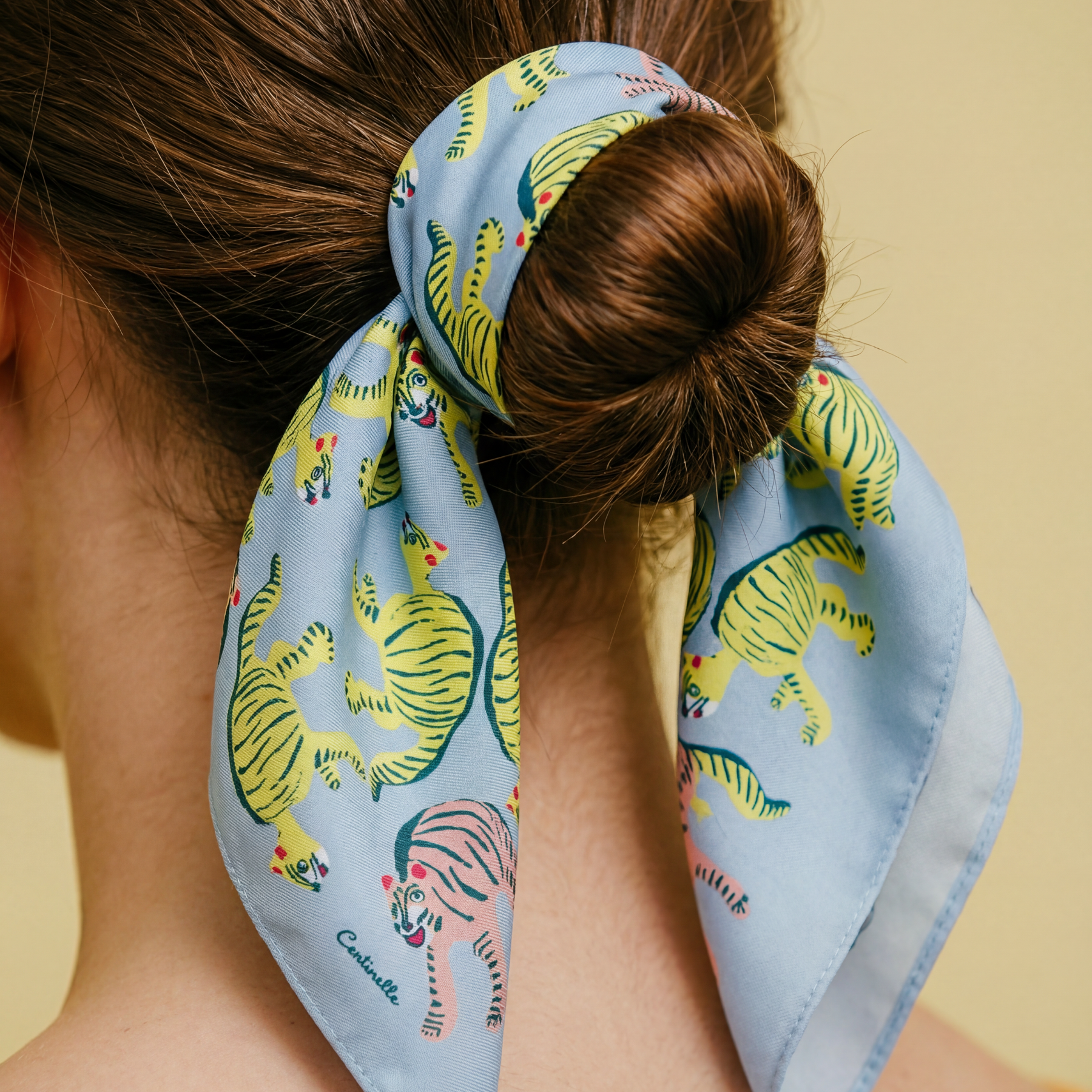 woman wearing a blue bandana in a bun with yellow tiger pattern on a yellow background